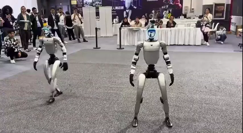 Two Unitree G1 robots performing a synchronized dance routine during a live capability demonstration