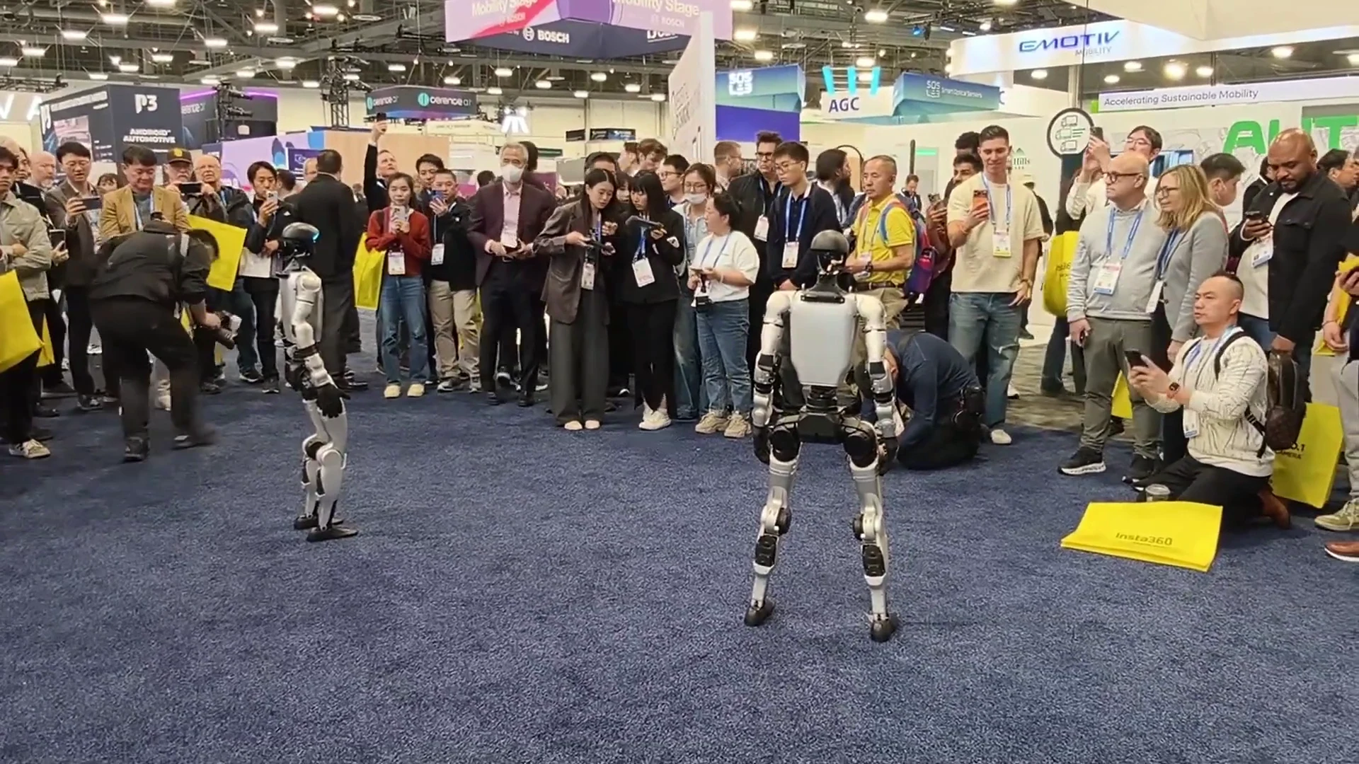 Two Unitree G1 robots at CES 2026 trade show engaging with a crowd of booth visitors