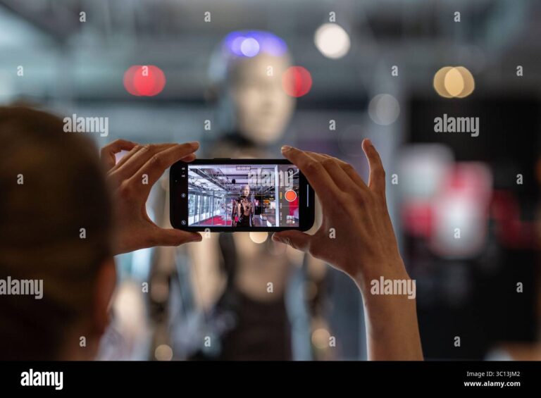 Visitor uses cell phone to record video of Ameca humanoid robot at museum exhibit