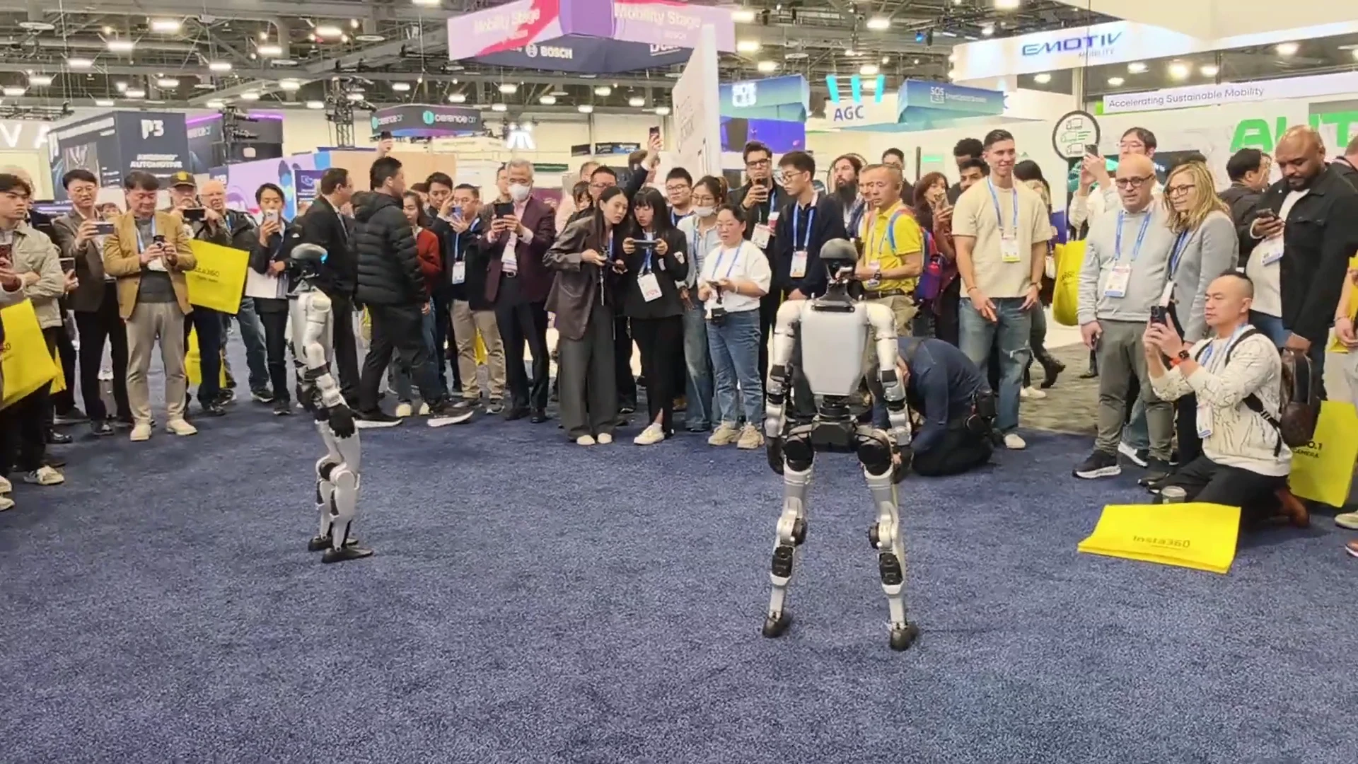 Two Unitree G1 robots at a trade show booth with attendees watching the live robot demonstration
