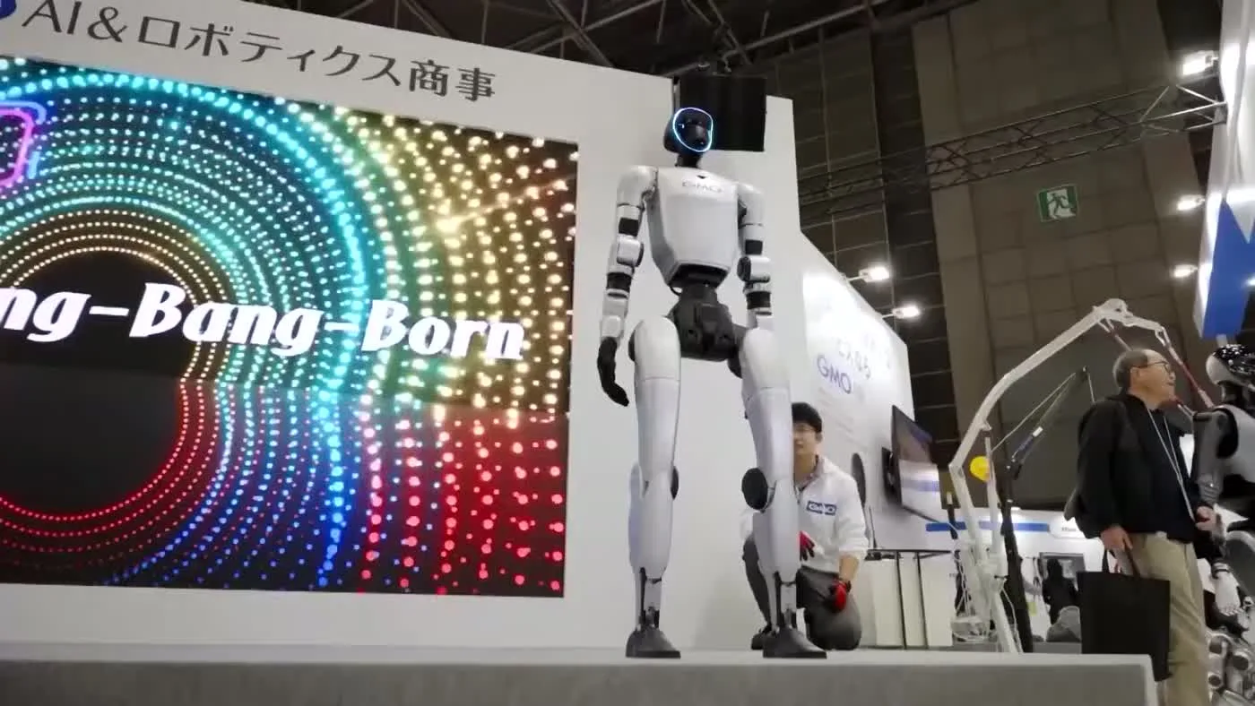 Unitree G1 robot standing at an international tech expo booth surrounded by spectators and display screens