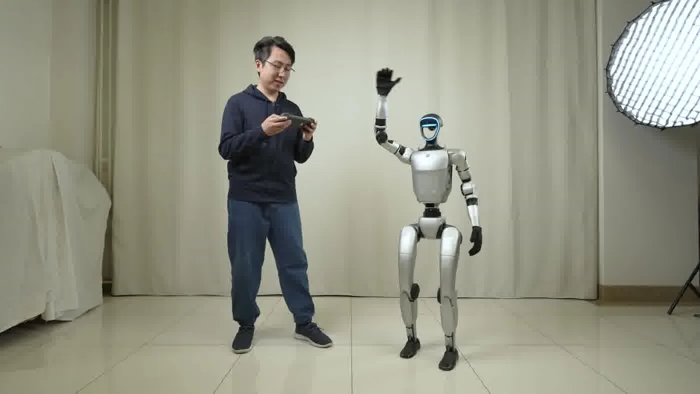 Operator using a tablet controller while the Unitree G1 humanoid robot raises its arm during a test session