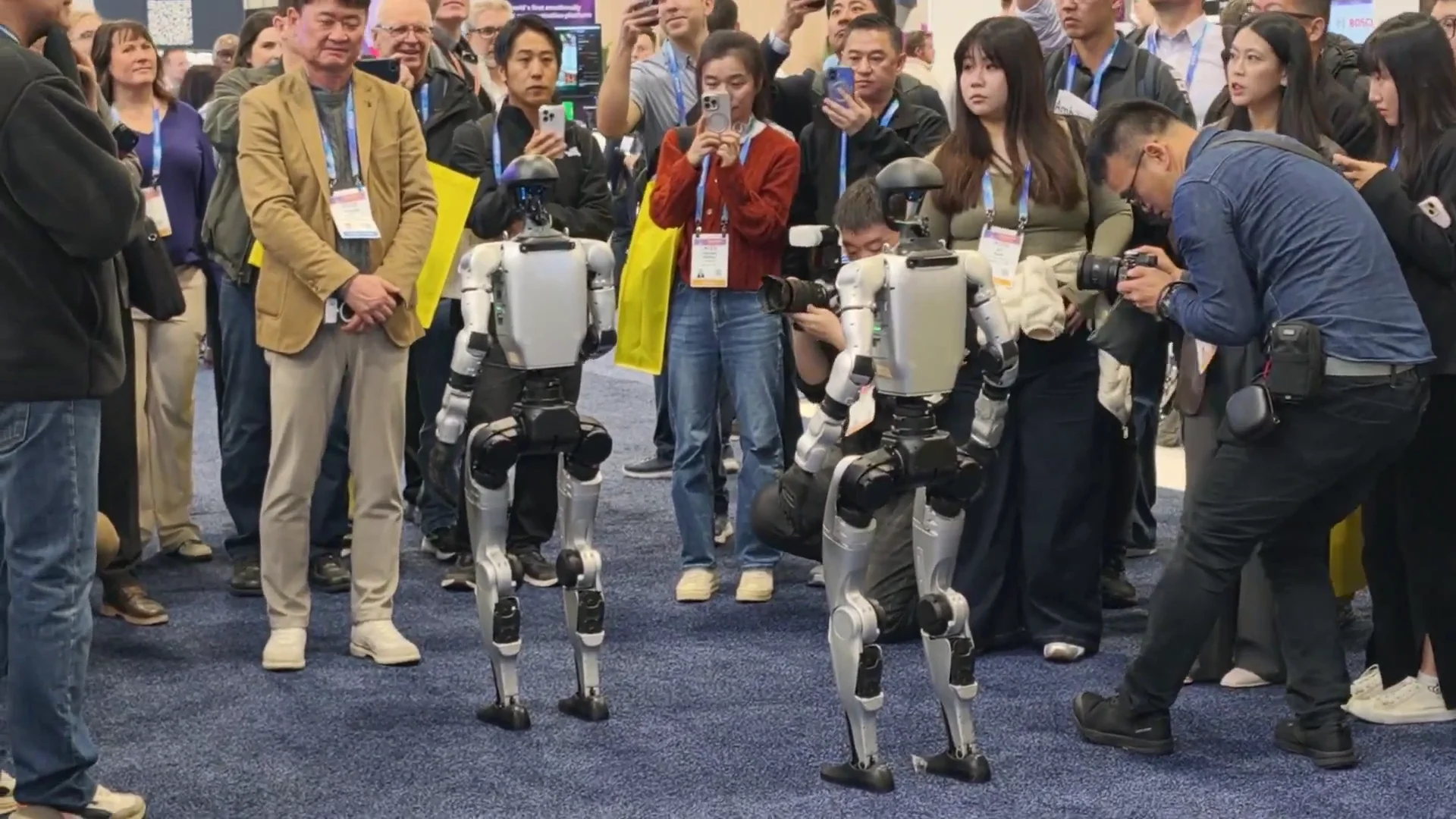 Two Unitree G1 humanoid robots surrounded by a crowd at a trade show, capturing live audience engagement at an event