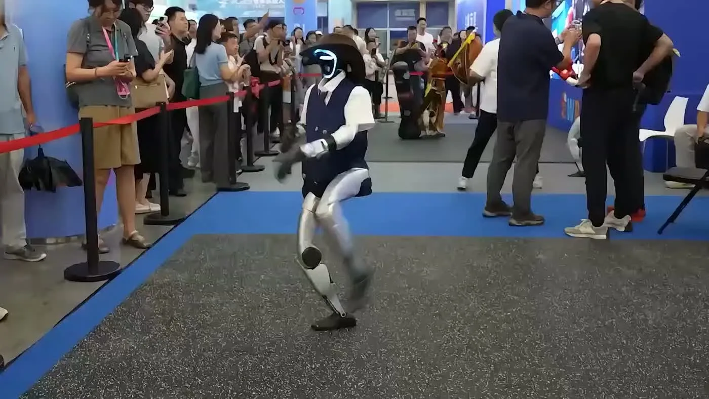 Unitree G1 humanoid robot performing a dance move at an indoor trade show event with a large crowd watching