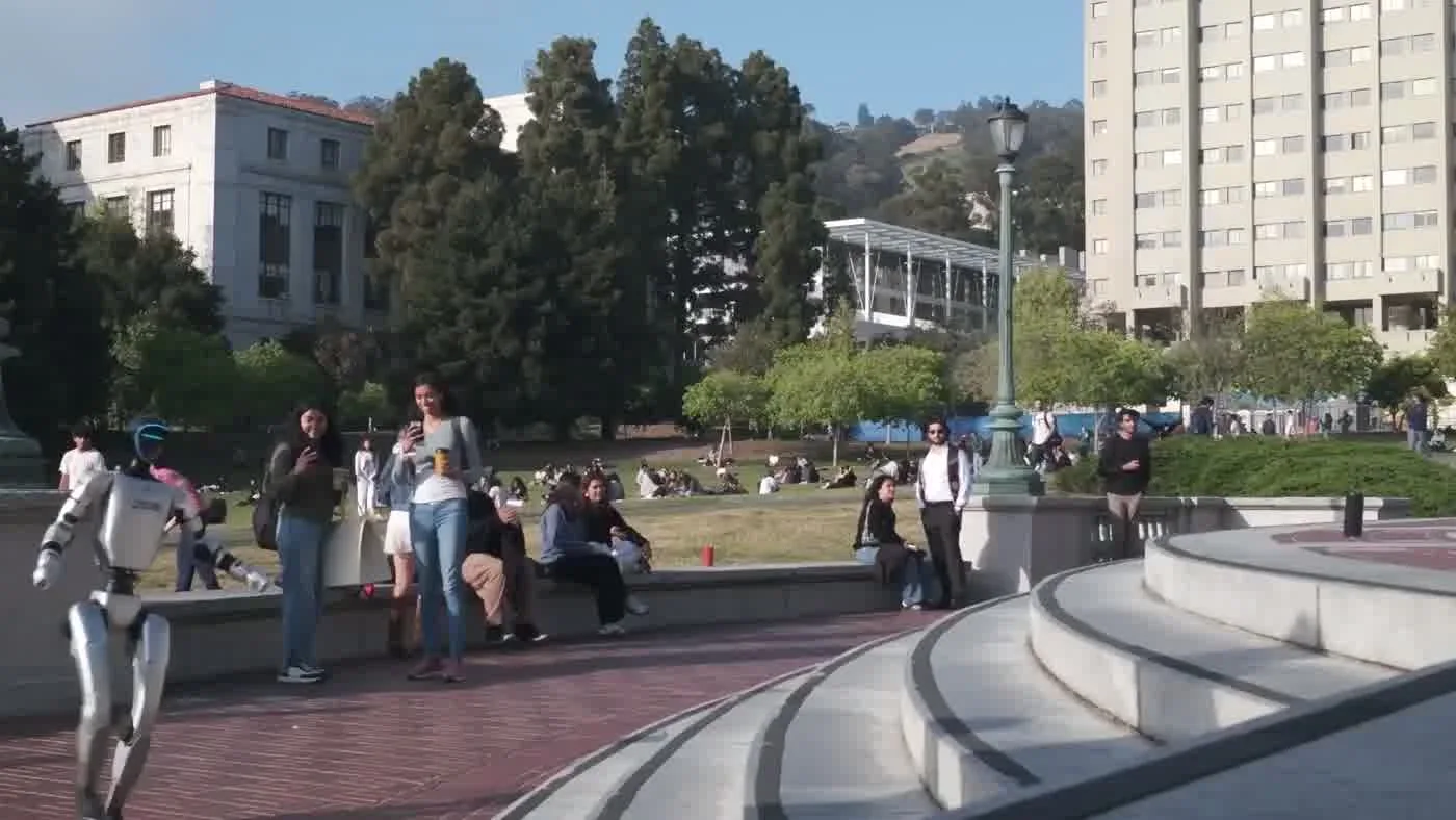 Unitree G1 humanoid robot walking across a university campus plaza alongside students on a sunny afternoon