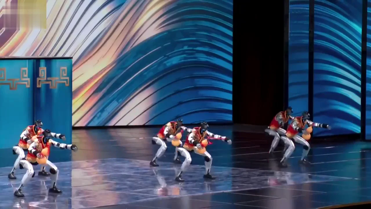 Multiple Unitree G1 robots in colorful costumes performing a synchronized dance on a large stage