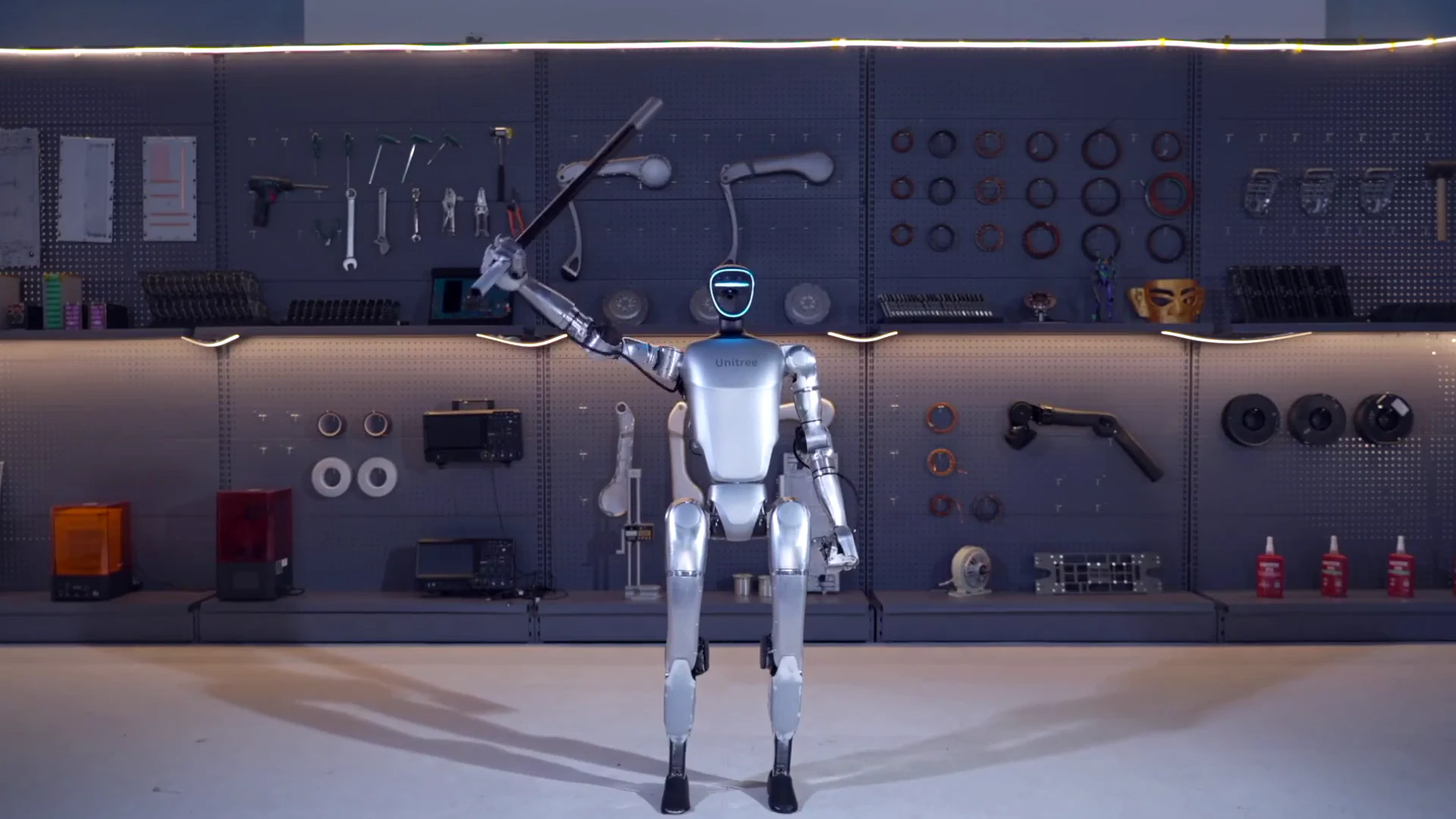 Unitree G1 robot standing upright in a workshop setting with tools and engineering components on the wall